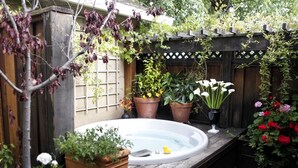 A hot tub in a garden with wooden fencing, potted plants, and flowering shrubs. - Mount View Hotel & Spa (Calistoga)