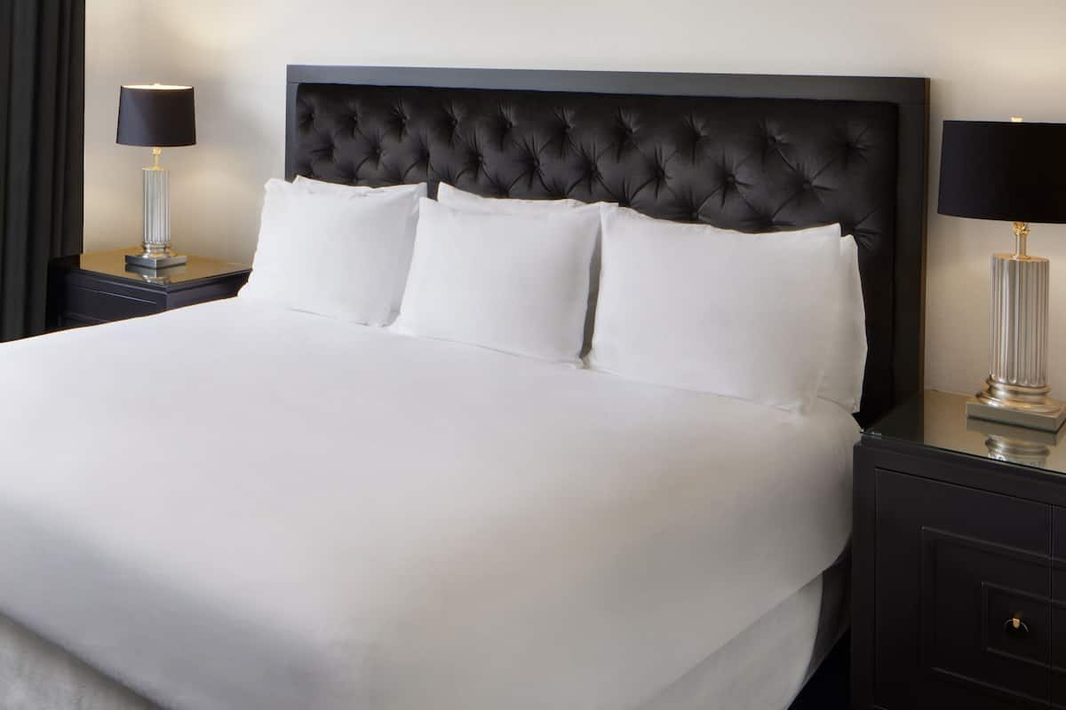A neatly made bed with a tufted headboard, two bedside tables with lamps, and a plain wall.