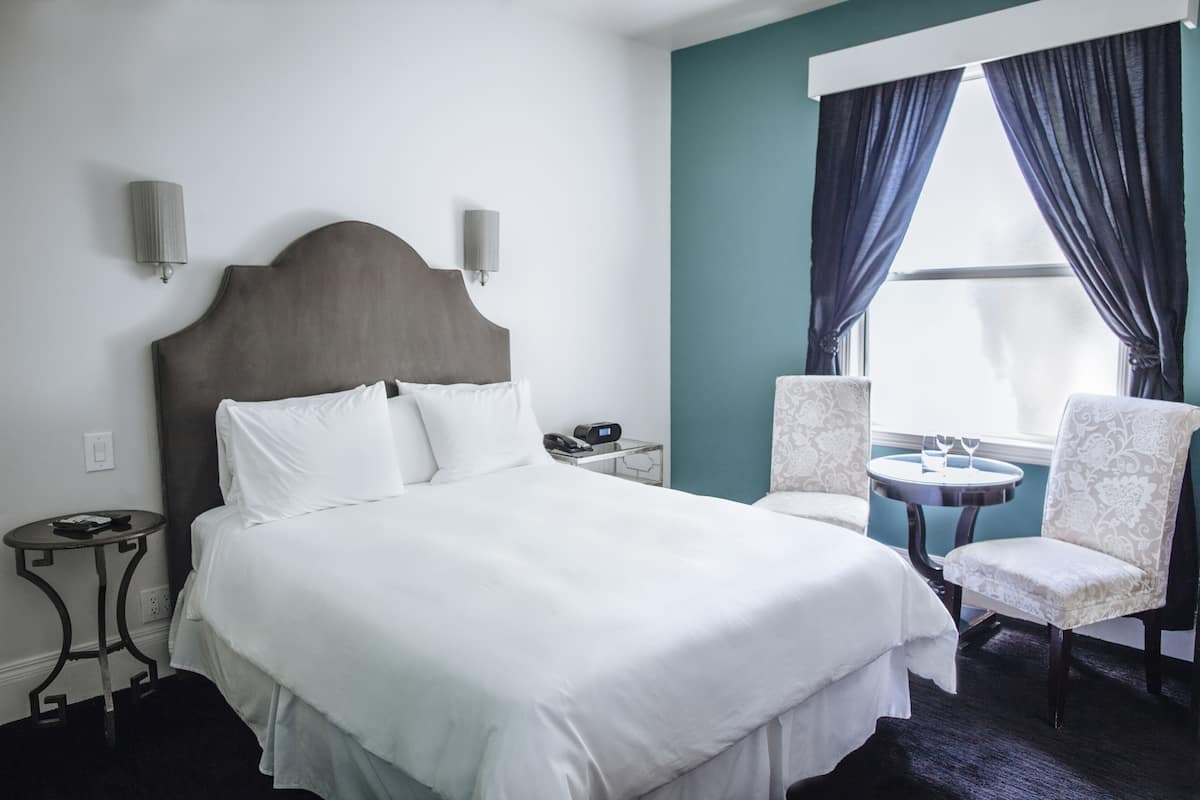 A hotel room with a large bed, two bedside tables, a chair, and a small table with a lamp.