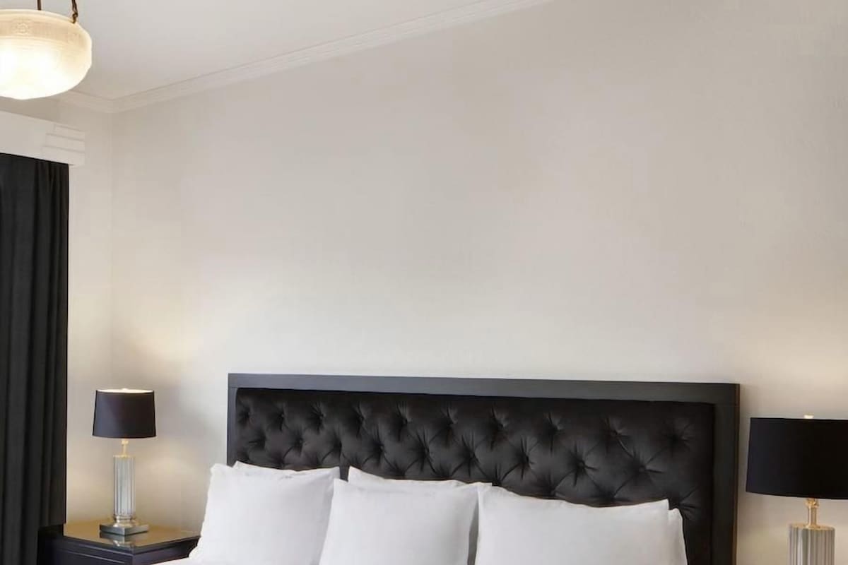 A neatly made bed with a tufted headboard, two bedside tables with lamps, and a plain wall.