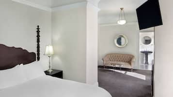 A hotel room with a large bed, a nightstand with a lamp, a sofa, a round mirror, and a television mounted on the wall.