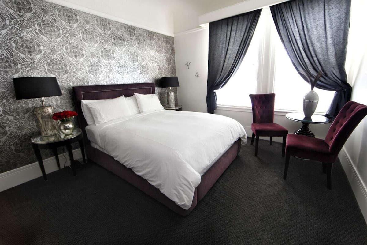 A hotel room with a large bed, two bedside tables with lamps, a chair, and a small table with a vase of flowers.