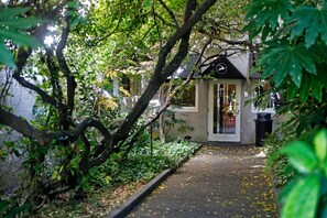 Un étroit sentier mène à un bâtiment doté d’une porte en verre, qui est entouré d’une végétation luxuriante et d’arbres.