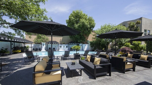 An outdoor patio area with seating arrangements, umbrellas, and a pool. - Mount View Hotel & Spa (Calistoga)