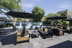 Un patio al aire libre con mobiliario, sombrillas y una piscina.