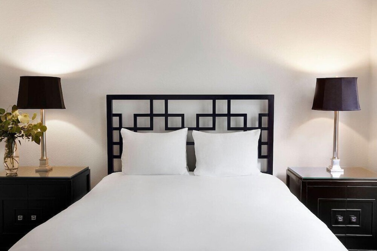 A neatly made bed with a black headboard, two bedside tables with lamps, and a vase with a plant on one table.