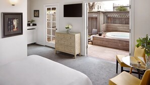 A hotel room with a bed, a dresser, a TV, and a view of an outdoor hot tub and deck. - Mount View Hotel & Spa (Calistoga)
