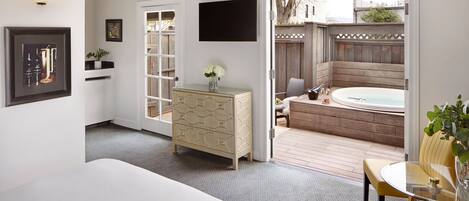 A hotel room with a bed, a dresser, a TV, and a view of an outdoor hot tub and deck.