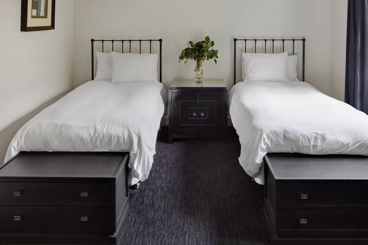 A twin room with two beds, a nightstand with a vase of flowers, and a framed picture on the wall.
