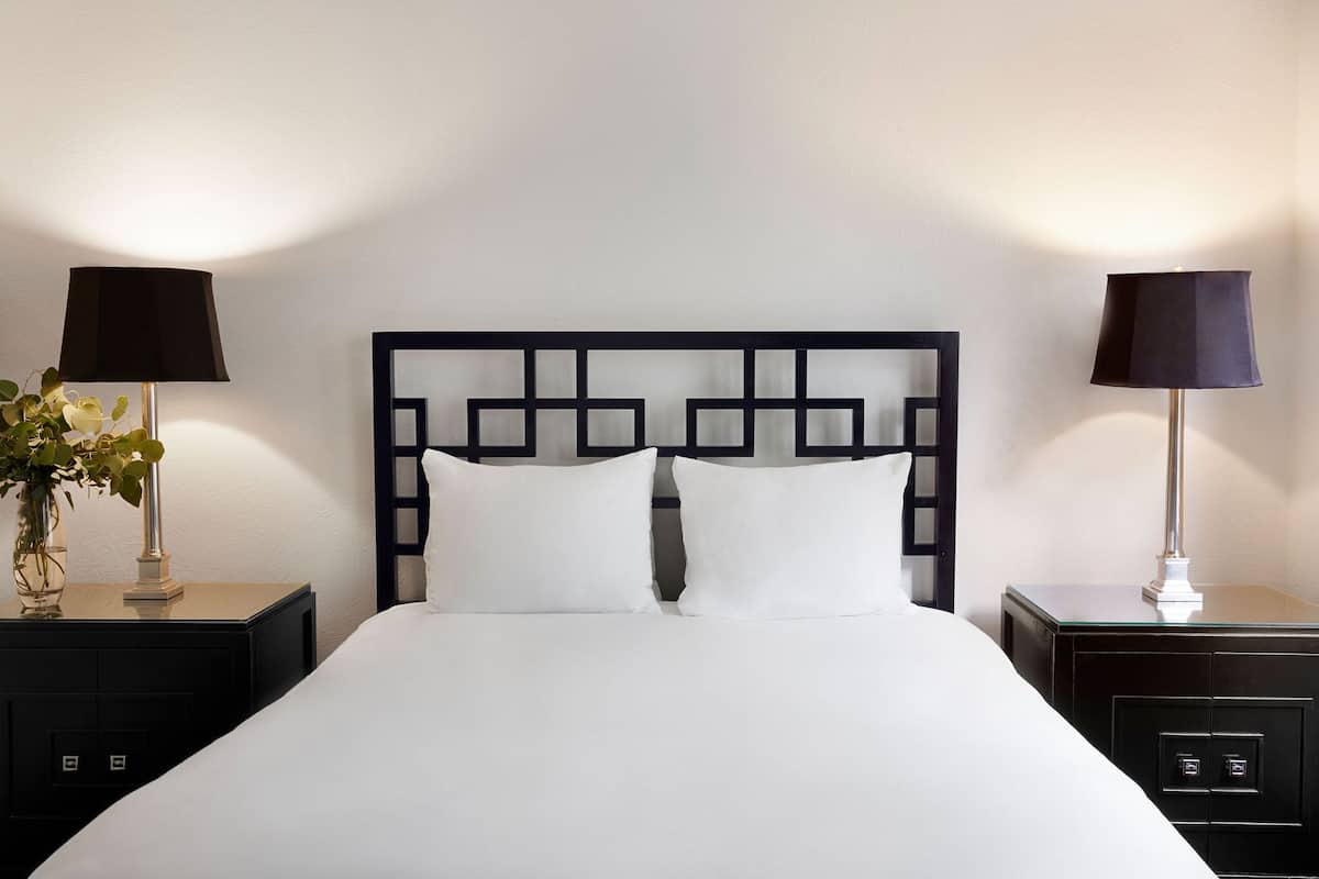 A neatly made bed with a black headboard, two bedside tables with lamps, and a vase with flowers on the left table.