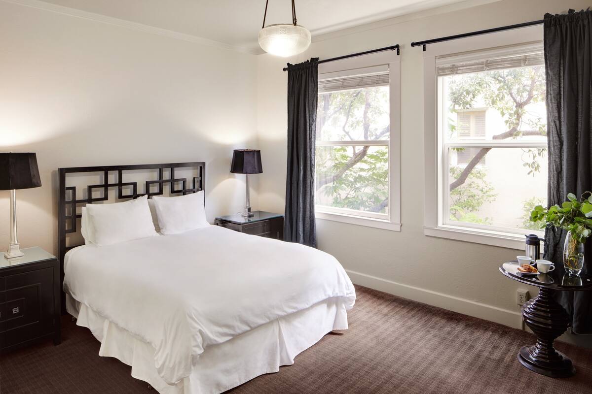 A neatly arranged bedroom with a bed, bedside tables, a lamp, and a window with curtains.