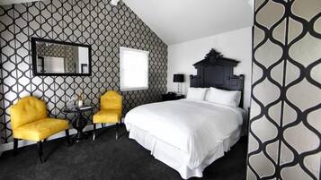 Ein Hotelzimmer mit einem großen Bett, zwei gelben Sesseln, einem kleinen Tisch, einem Spiegel und einer Wand mit Muster.