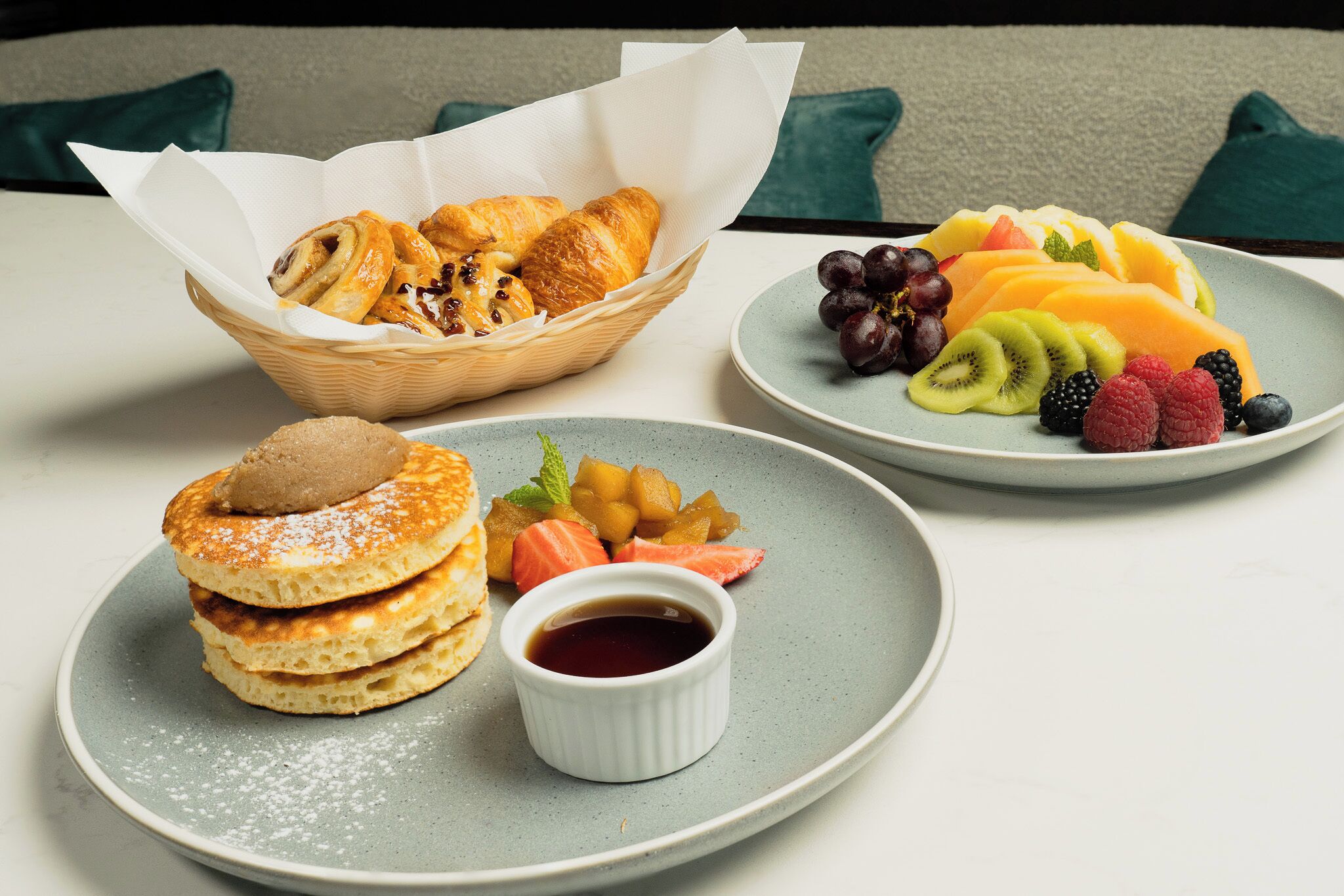 Een ontbijttafel met gebak, fruit en pannenkoeken op borden.