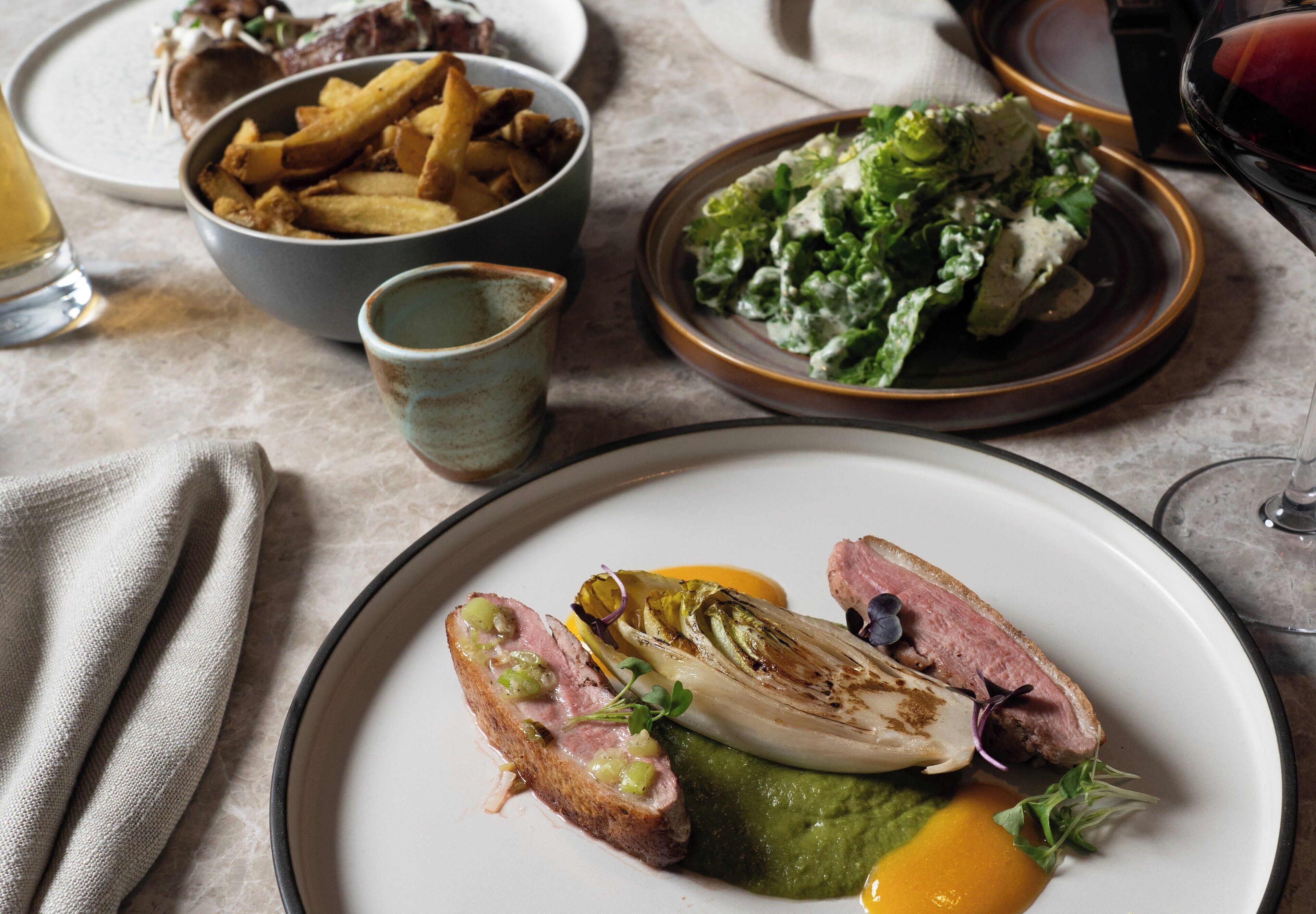 Una mesa de comedor con platos de comida, incluyendo un bistec, un vegetal verde y una ensalada.
