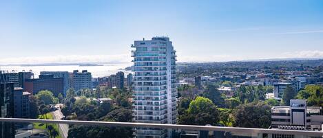 A high-rise building with multiple balconies, surrounded by other buildings and greenery, viewed from a distance.