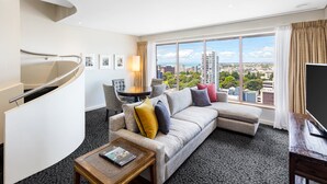 A modern hotel room with a curved staircase, a large window with a city view, a sofa with cushions, a coffee table, and a flat-screen TV. - Crowne Plaza Auckland by IHG (Auckland)