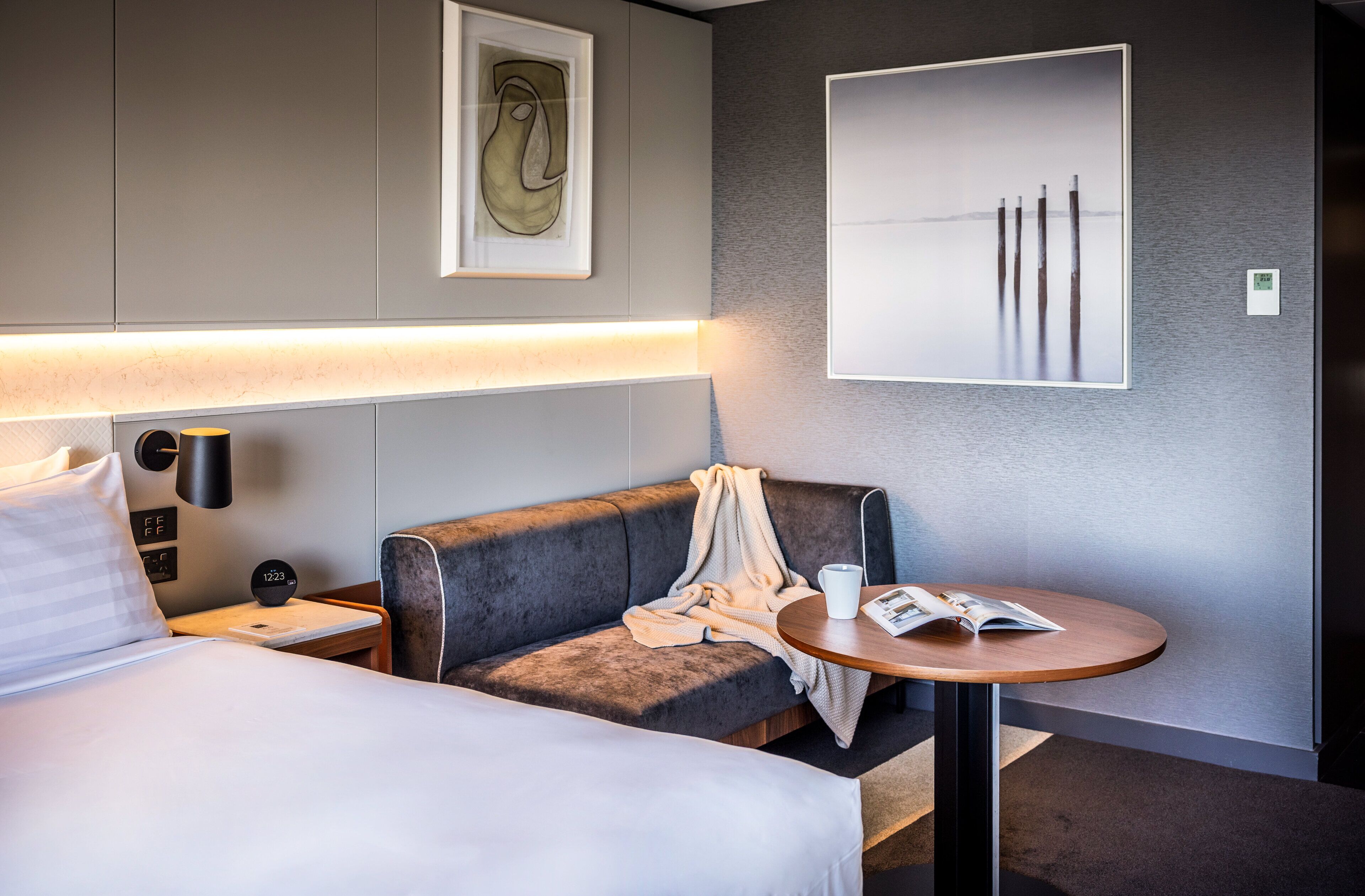 Une chambre d’hôtel comprenant un lit, un canapé, une petite table, une horloge murale et des œuvres d’art.