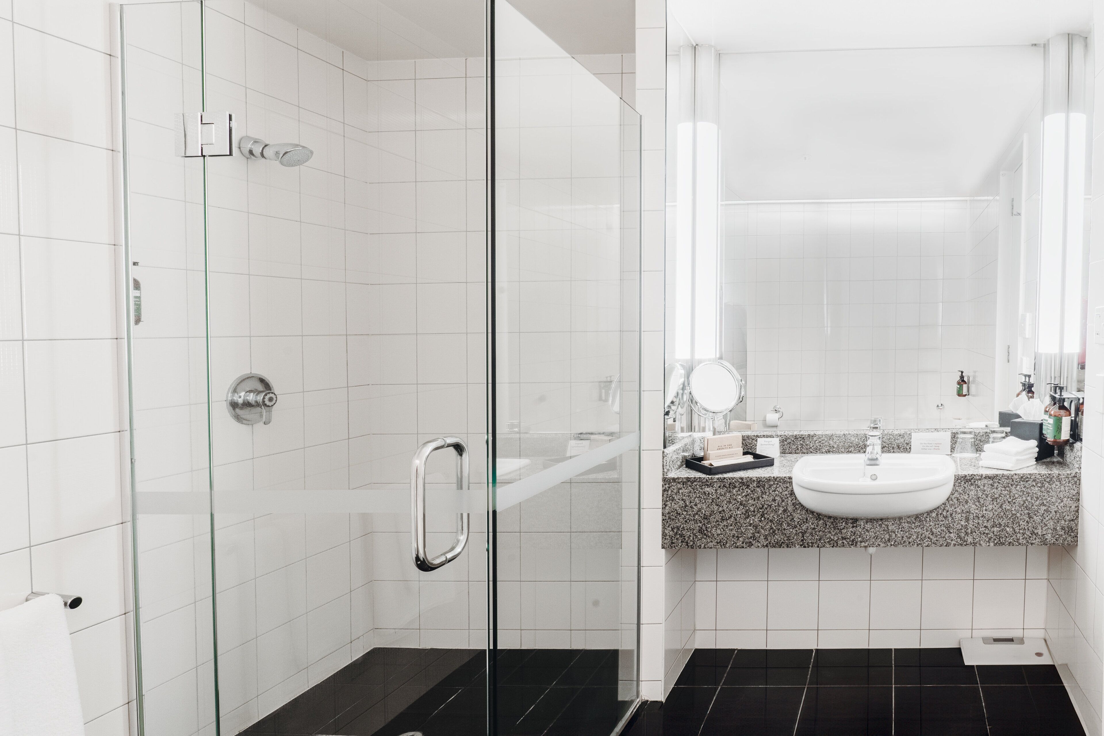 A modern bathroom with a glass shower enclosure, a granite countertop sink, and a large mirror.
