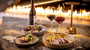 A dining table with plates of food, wine glasses, and a bottle of wine.