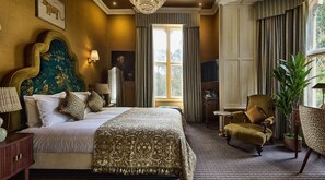A hotel room with a large bed, a sitting area with a chair, a small table, a TV, and a window with curtains.