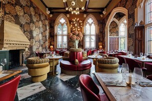 Een restaurant met ronde tafels, rode stoelen en een open haard.