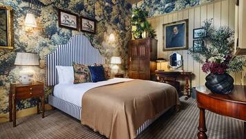 A room with a bed, a wooden cabinet, a desk, and a wall with floral wallpaper.