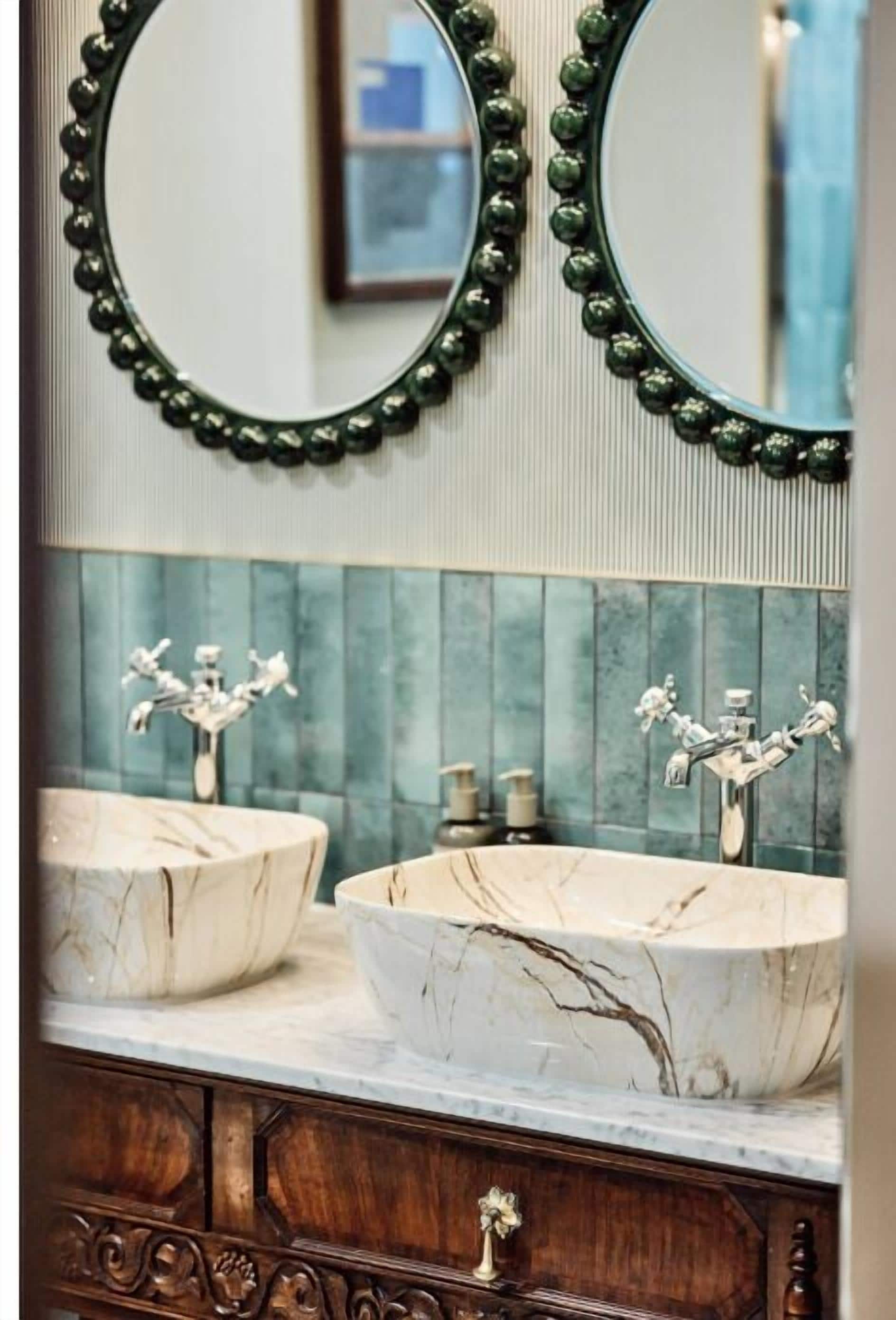 A bathroom with two marble sinks, a wooden vanity, and a mirror with a green bead frame.