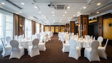 Un salón de banquetes con mesas redondas dispuestas para un evento formal, con sillas blancas, vajilla y candelabros con velas.