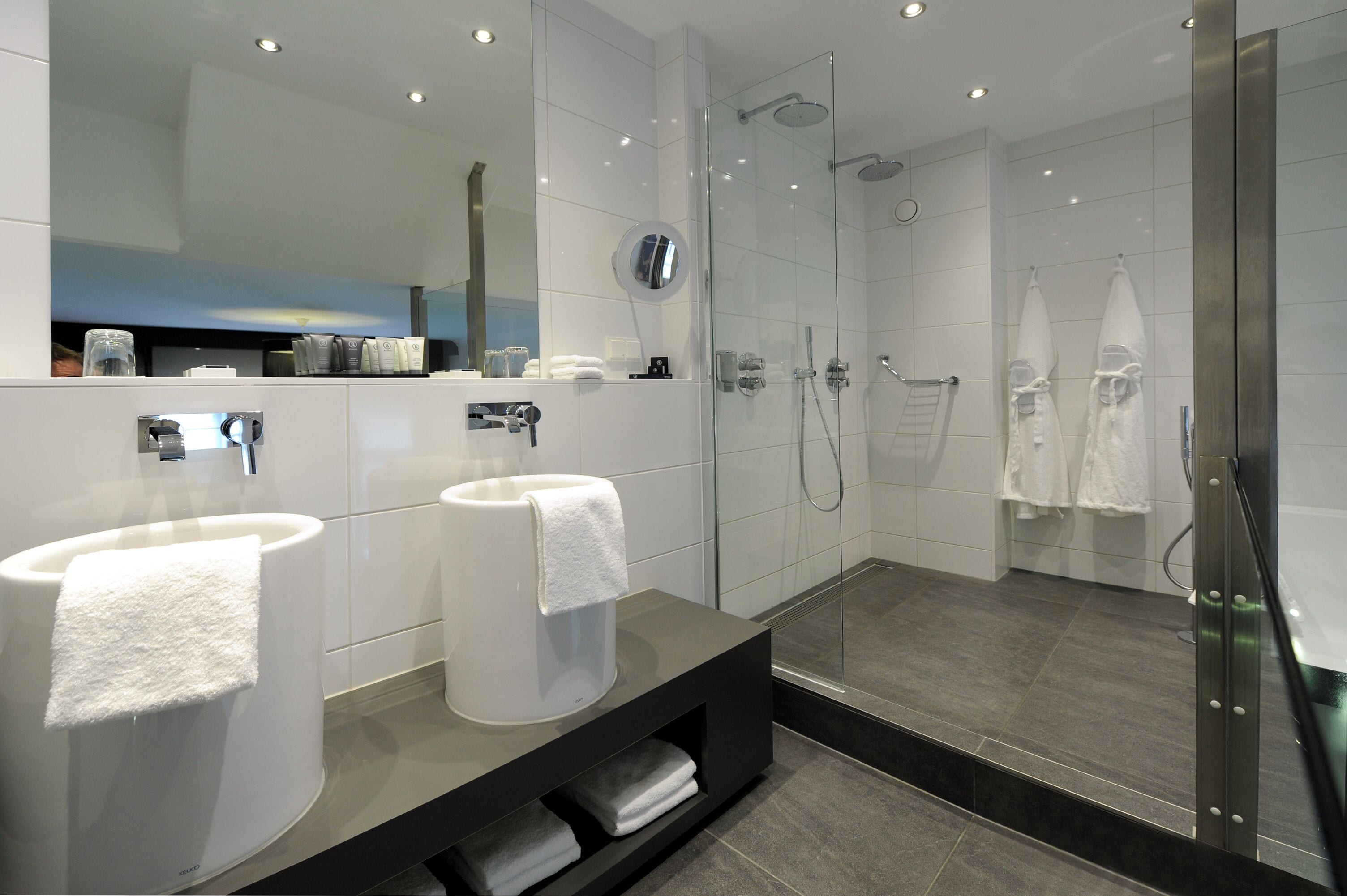 A modern bathroom with two sinks, a glass shower enclosure, and a large mirror.