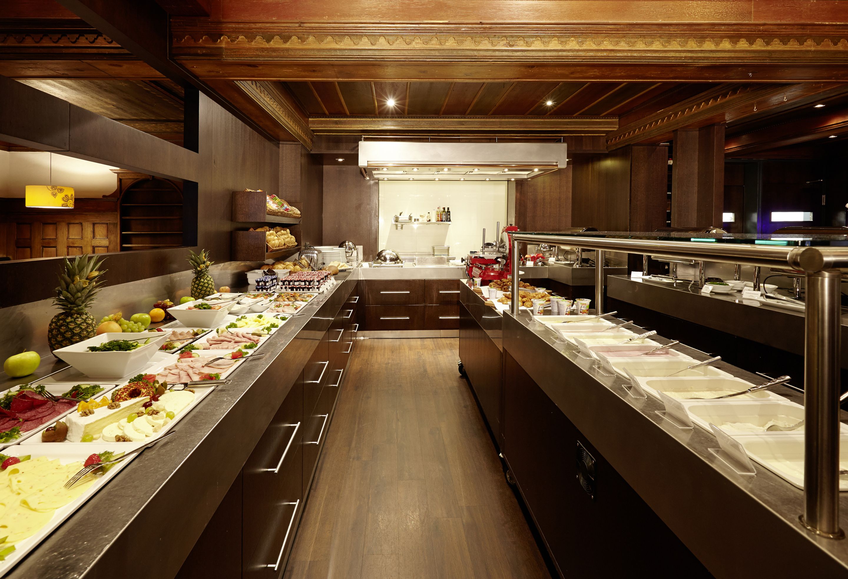 Ein Buffet mit verschiedenen Speisenstationen, Holzvertäfelung und einem modernen Küchenbereich im Hintergrund.