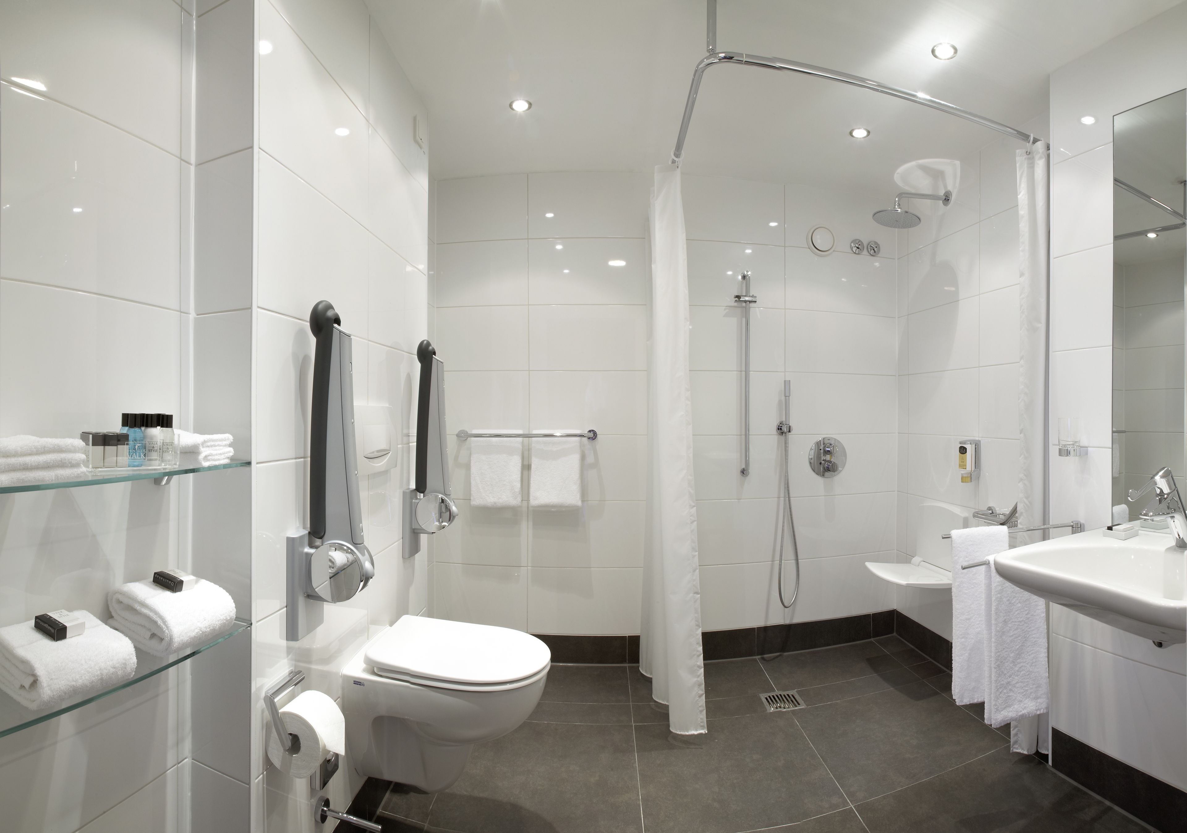 Une salle de bain moderne avec une douche à parois de verre, des toilettes, un lavabo et une étagère en verre où sont posées des serviettes.