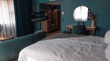 A hotel room with a large bed, a seating area, a vanity with a mirror, and a wardrobe.