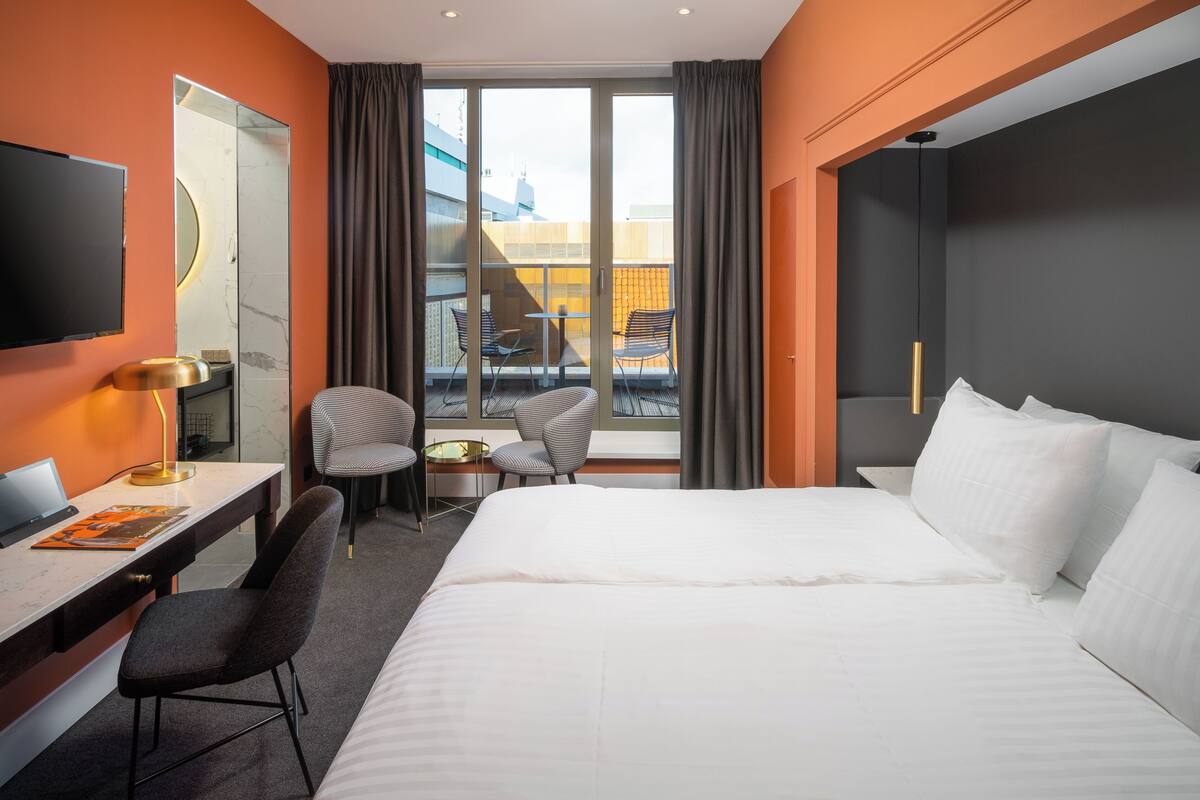 Une chambre d’hôtel avec un grand lit, un bureau avec un ordinateur portable, une chaise, une petite table et un balcon avec des chaises.