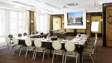 A conference room with a long table, chairs, a projector screen, and a large window with curtains.