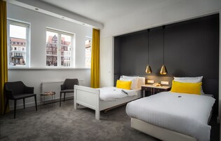 A hotel room with two beds, a sitting area with chairs, a small table, and a view of buildings through large windows.
