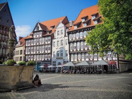 Una plaza adoquinada con edificios históricos, una estatua y zonas de estar al aire libre.