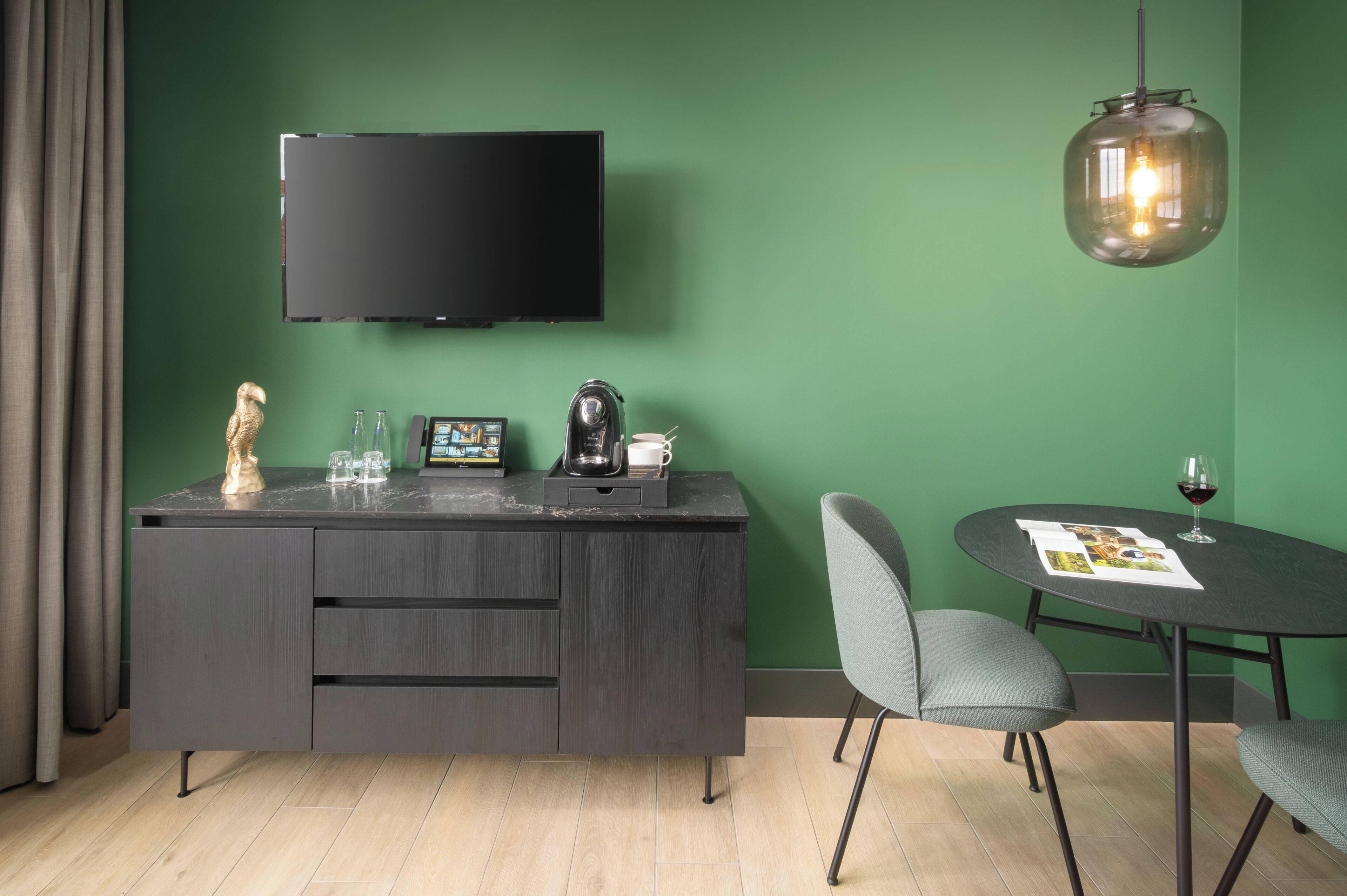 Ein modernes Zimmer mit einem dunklen Holztisch, einem Flachbildfernseher, einer Pendelleuchte und einem runden Tisch mit Stühlen.