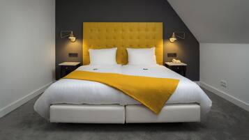 Un dormitorio moderno con un cabecero capitonado, una cama grande con ropa de cama blanca, una manta color mostaza y dos mesitas de noche con lámparas.