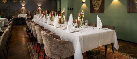 A long dining table with white tablecloths and chairs, set with plates, glasses, and flowers.