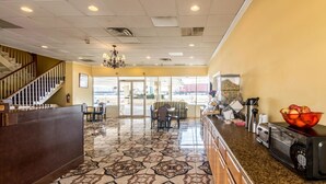 A lobby with a reception desk, a staircase, a chandelier, a patterned floor, a coffee machine, a microwave, and a bowl of fruit. - Rodeway Inn Arlington Entertainment District Area (Arlington)