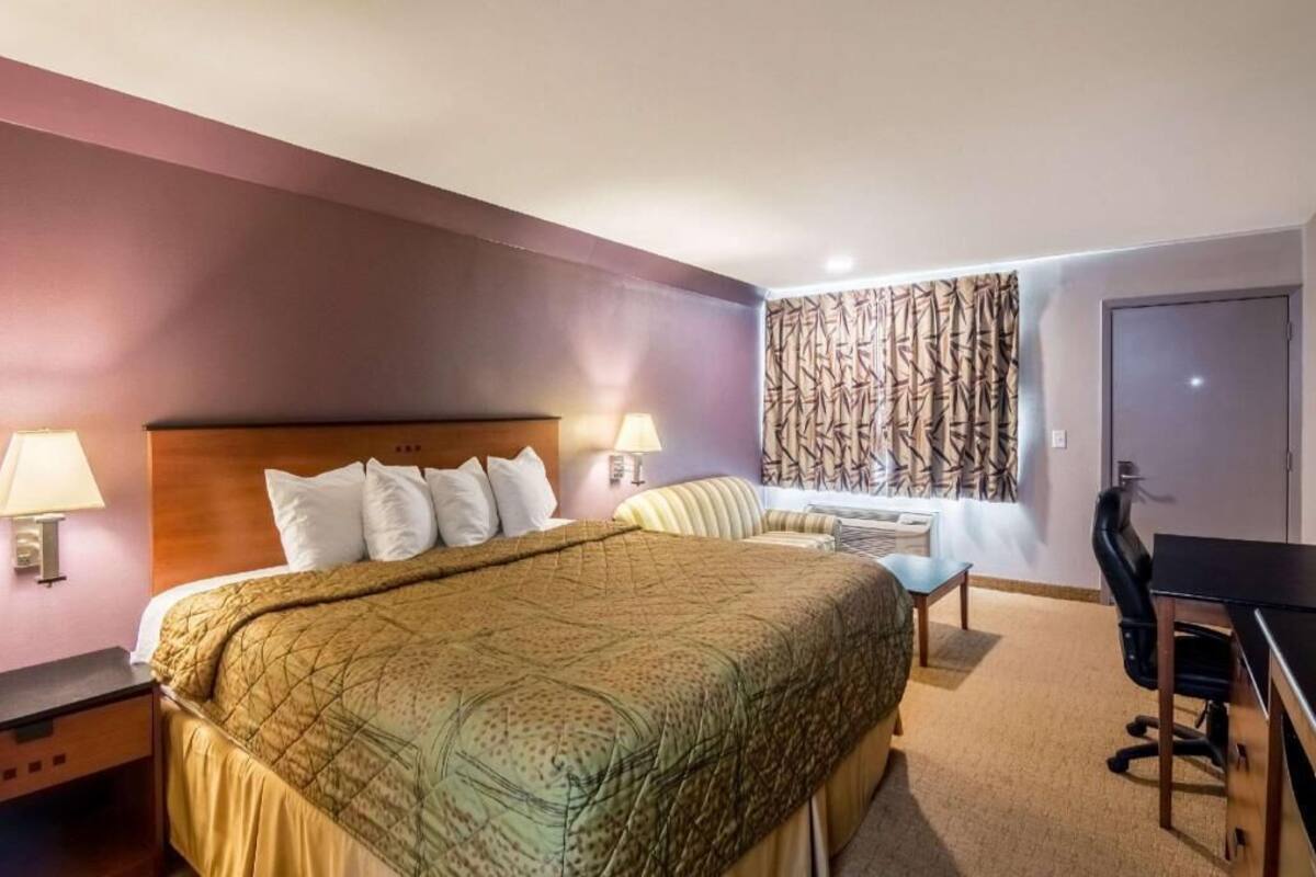 A hotel room with a bed, bedside lamps, a desk, a chair, and a patterned curtain.