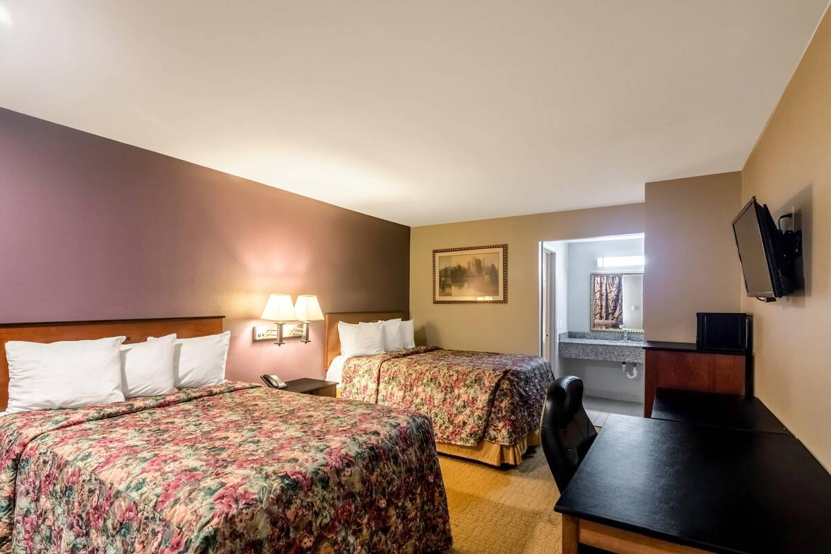 A hotel room with two beds, a desk, a chair, a TV, and a painting on the wall.