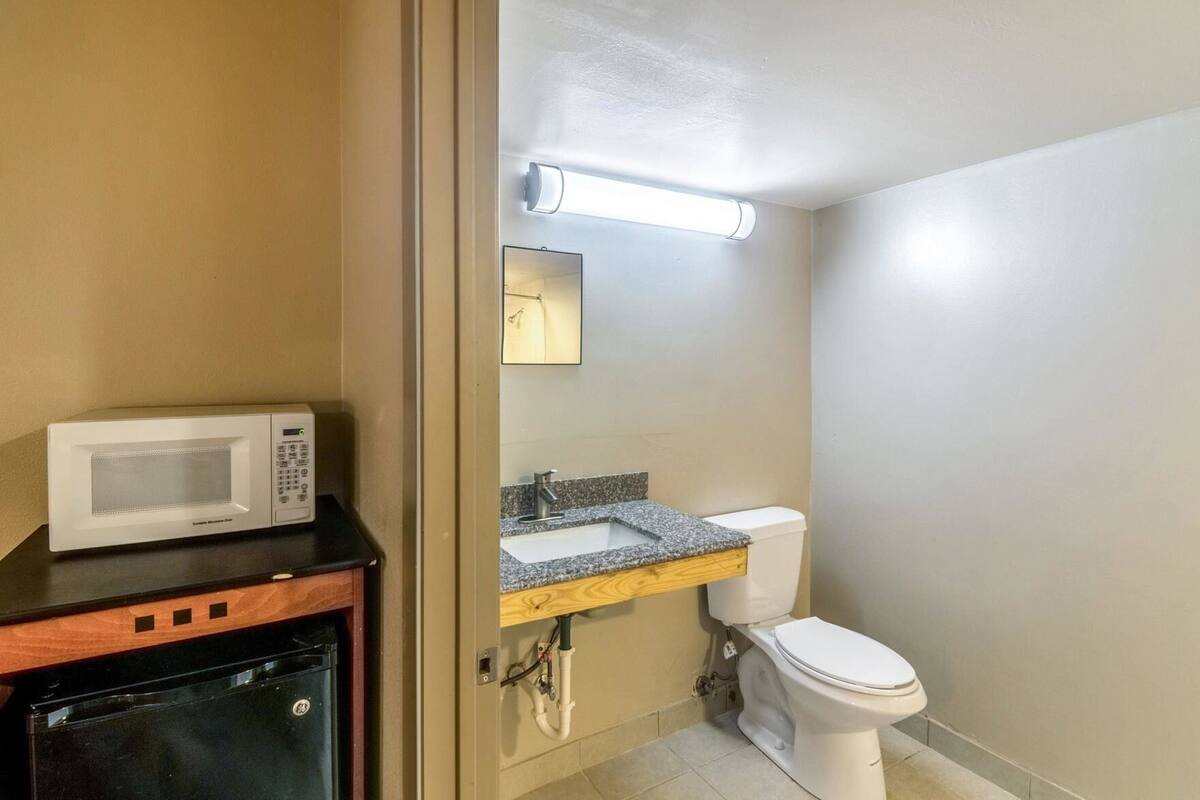 A compact bathroom with a microwave on a counter, a sink with a granite countertop, and a toilet.