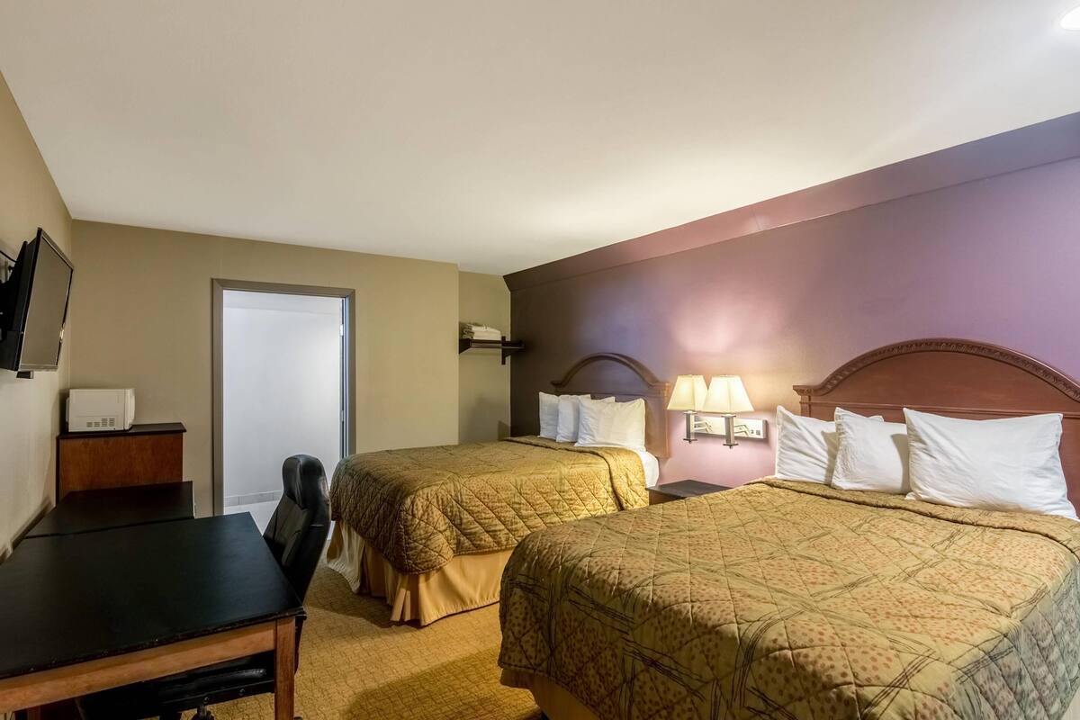 A hotel room with two beds, a desk, a chair, a TV, and a door.