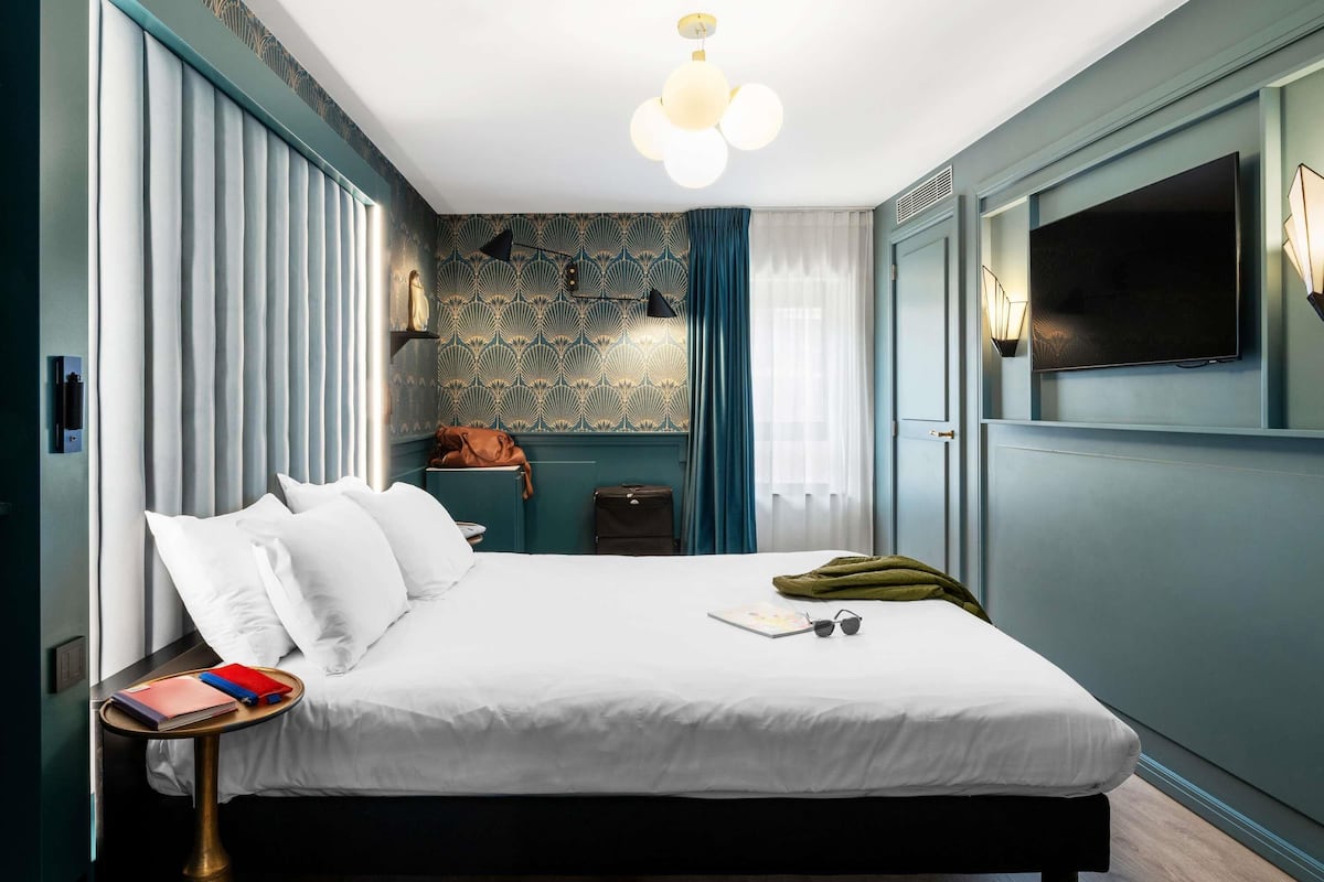 A modern hotel room with a large bed, bedside table, and a TV mounted on the wall.