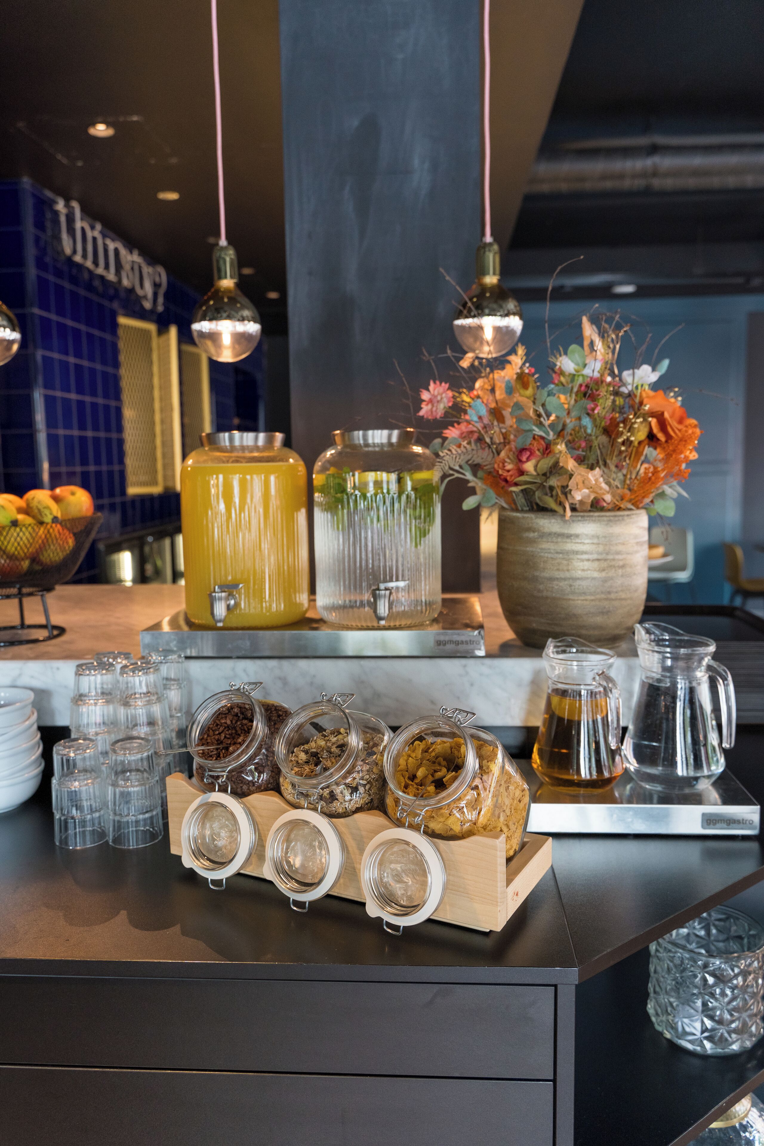 Una barra de desayuno con un frutero, un dispensador grande de jugo, un florero y varios recipientes de comida.