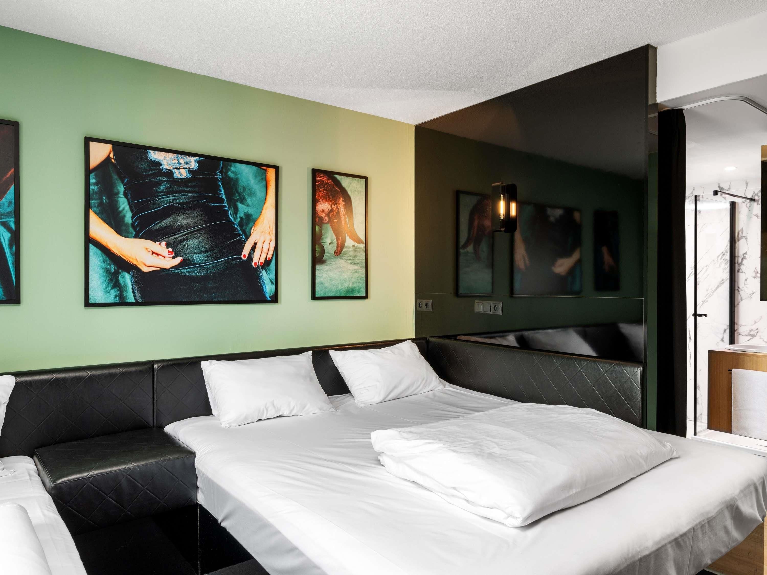 A modern hotel room with a large bed, a black leather sofa, and artwork on the walls.