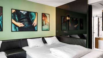 A modern hotel room with a large bed, a black leather sofa, and artwork on the walls.