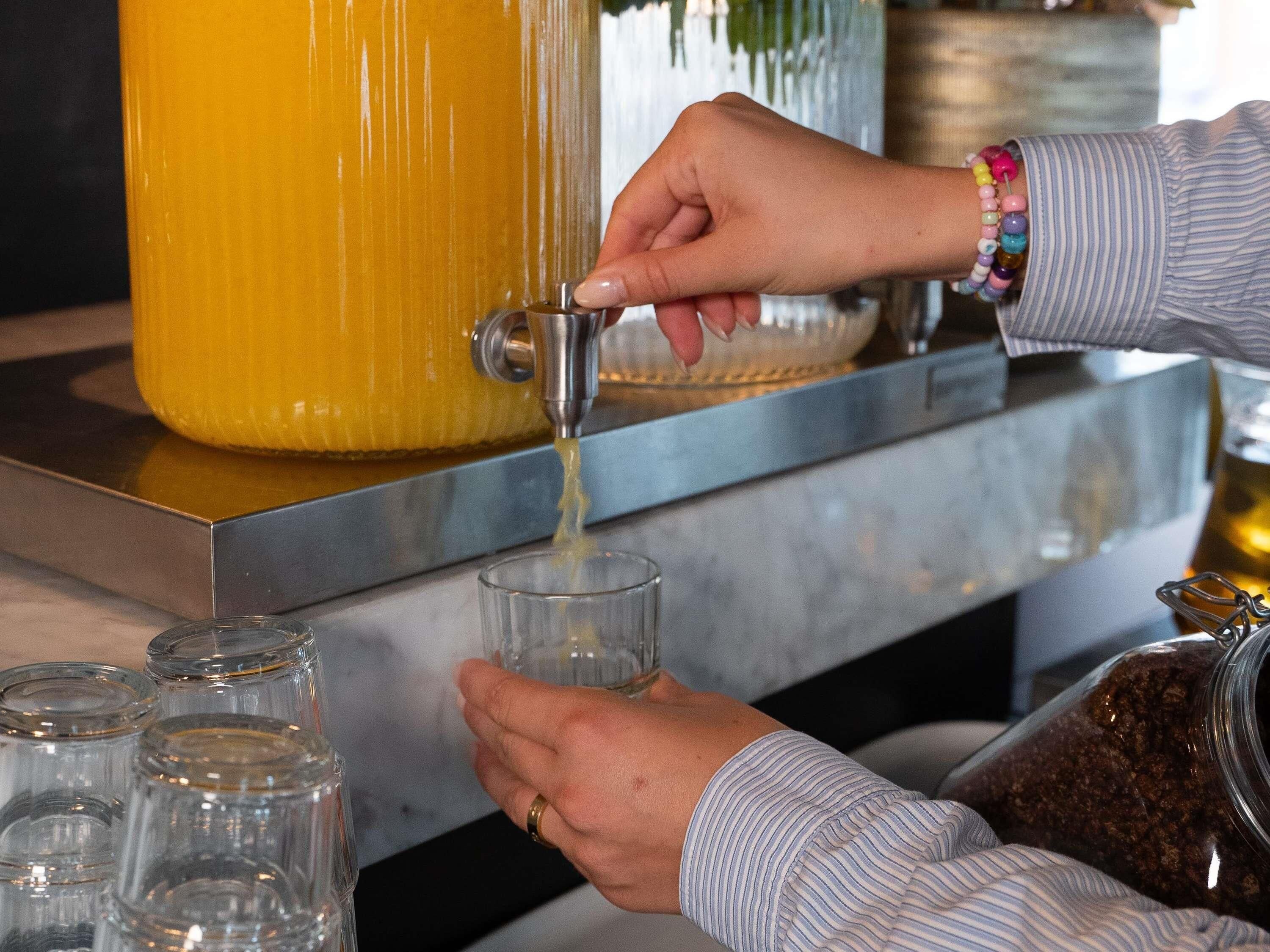 A hand pouring a yellow liquid from a tap into a glass.