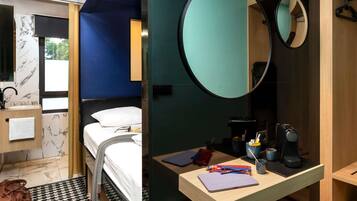 A modern hotel room with a bed, a round mirror, a wooden desk with a laptop, and a bathroom with a marble sink.